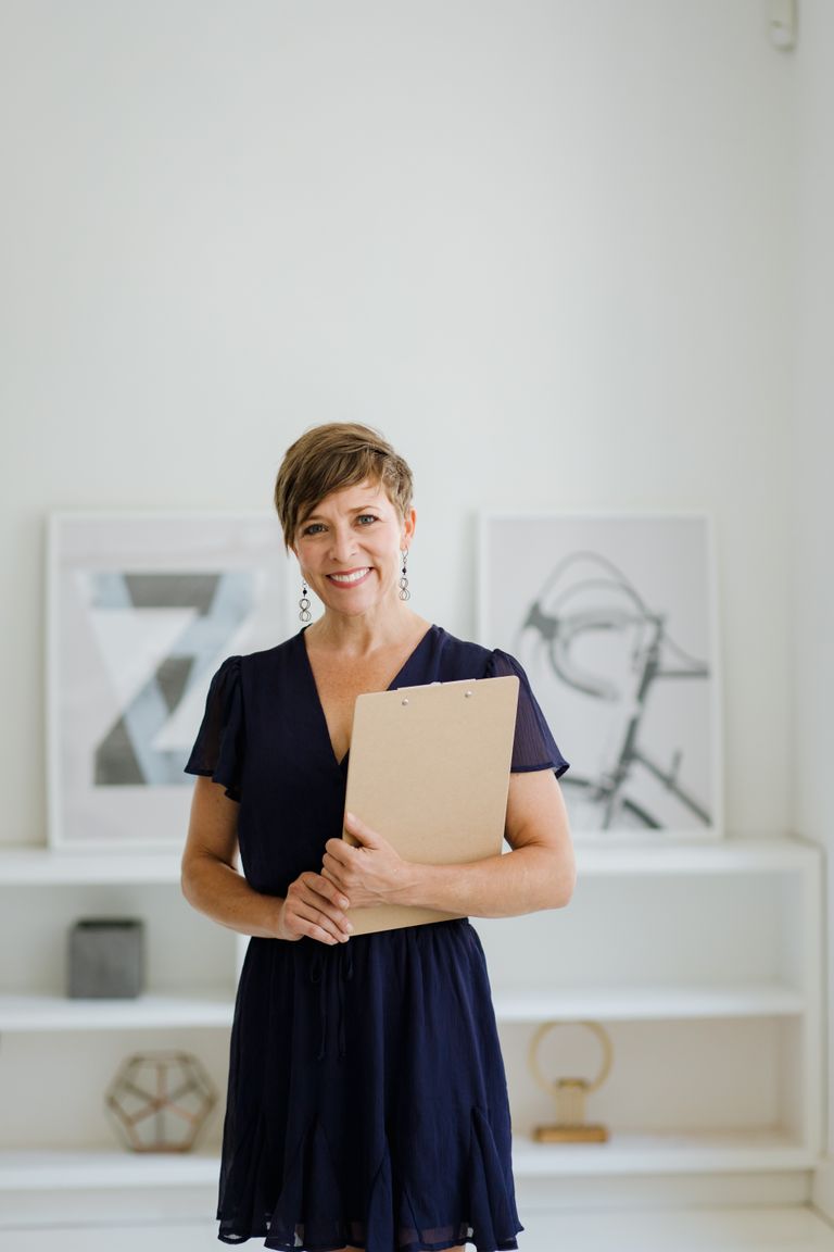Woman with short hair holding a clipboard in a minimalist indoor setting.